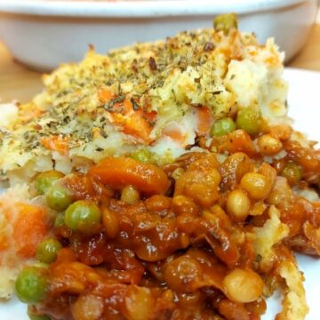 Portion of vegan shepherd’s pie on a white plate with rest of pie in the background