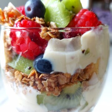 Fruit, yogurt and granola layer in a glass making Vegan Granola parfait